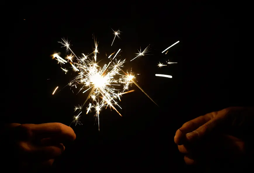 Two hands light sparklers on a dark background.