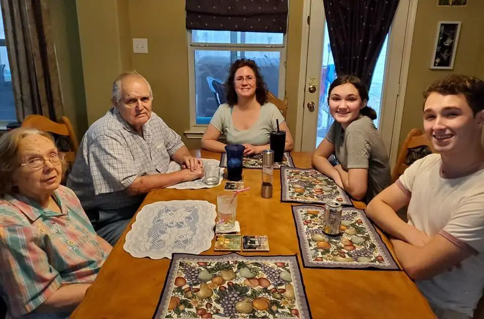 Multi-generational family sits around dining table and smiling at the camera.